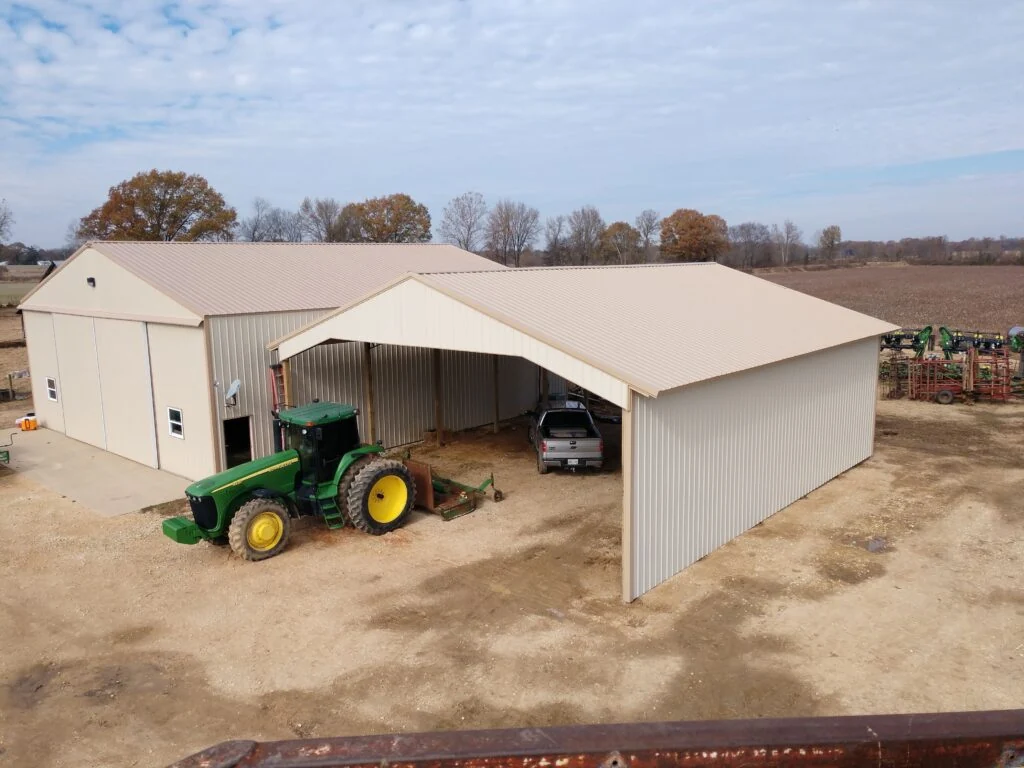 Farm equipment beside a metal barn with enclosed areas and a covered center bay